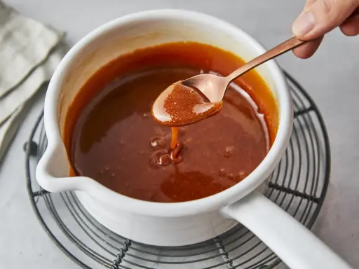 Flüssiges Karamell tropft von einem Löffel in einen Topf. Das Zucker karamellisieren ist fast perfekt.