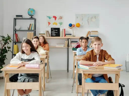 Schüler sitzen an Holztischen in einem hellen Klassenzimmer. Eine mögliche Sitzordnung für unruhige Klassen, die Konzentration fördert.
