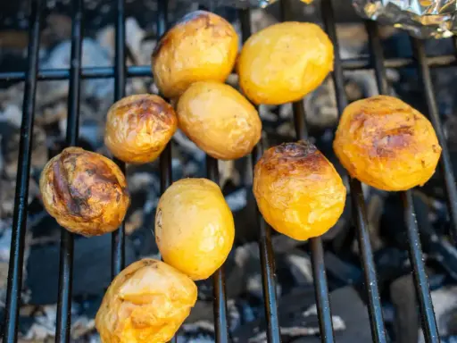 Kleine, goldbraune Kartoffeln garen auf dem Grillrost über glühender Kohle. Sie sind bereit für ein leckeres Abendessen.