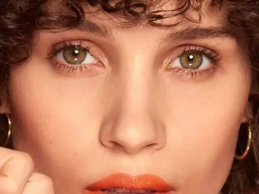 Primer plano de una mujer con rizos oscuros y maquillaje color coral vibrante en los labios.