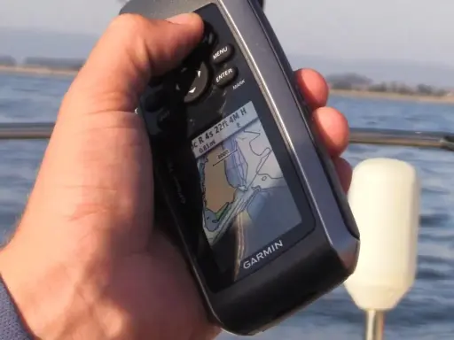 Main tenant une carte GPS Garmin sur un bateau, naviguant sur l'eau.
