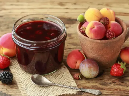 Ein Glas selbstgemachte Marmelade mit frischen Früchten daneben. Die Frage "wie lange ist selbstgemachte Marmelade haltbar" beschäftigt viele Hobbyköche.