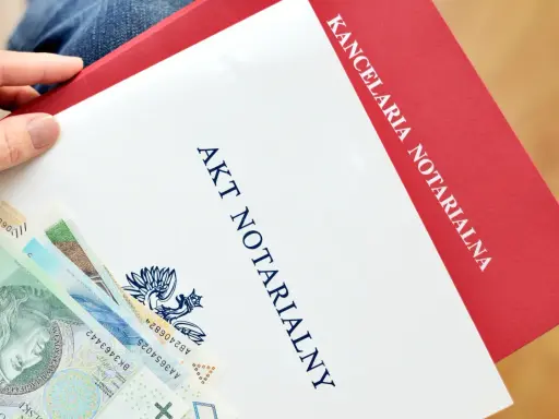 Ręka trzyma dokument "Akt notarialny" z banknotami. Kancelaria notarialna przygotowuje ważne dokumenty.