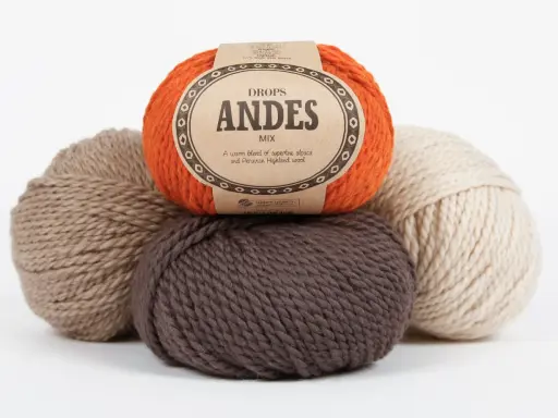 Kłębek pomarańczowej włóczki DROPS Andes, obok brązowych i beżowych kłębków. Idealna na ciepłe projekty.