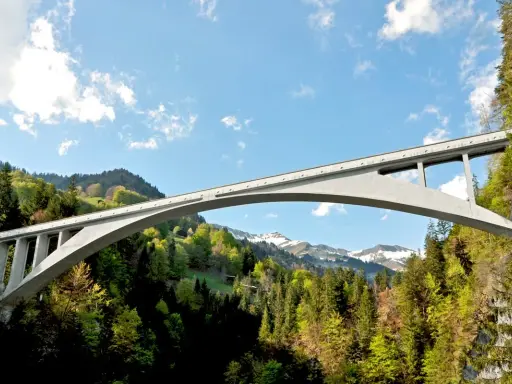 El puente de Salginatobel se alza majestuoso sobre un valle verde, con picos nevados al fondo.