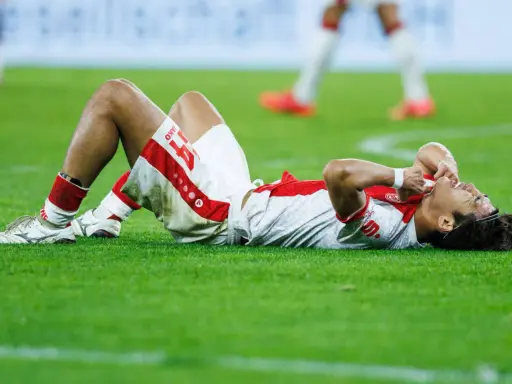 Fußballer liegt erschöpft auf dem Rasen, die Hände im Gesicht. Nach einem harten Spiel braucht er Regeneration.