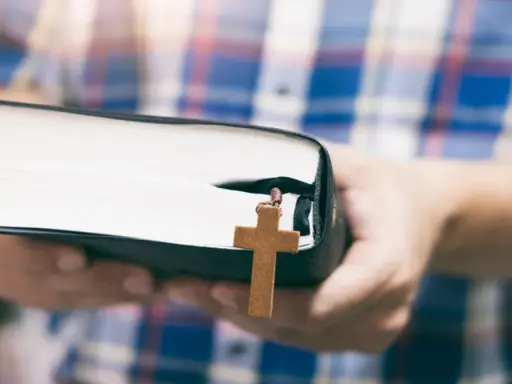 Osoba w kratę trzyma Biblię z drewnianym krzyżem, symbolizującym dwa przykazania miłości.