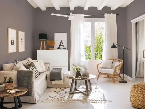 Salones pequeños con encanto: un sofá beige, sillón de mimbre, mesas de madera y detalles decorativos crean un espacio acogedor.