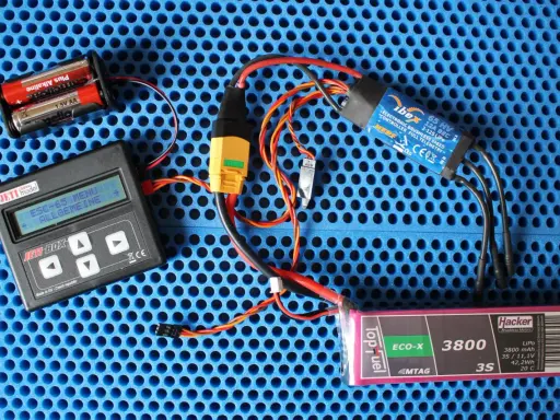 Jeti Box mit ESC-65-Menü, ibex 65 HV ESC, Hacker LiPo-Akku und Batterien auf blauem Untergrund.