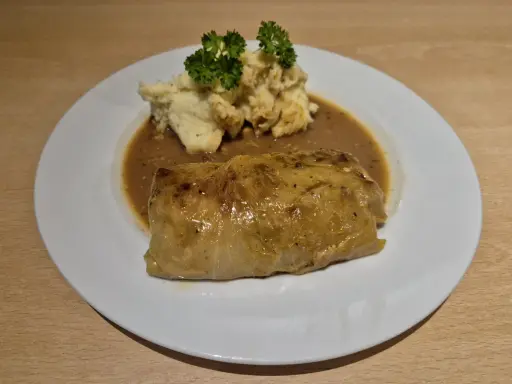 Ein herzhaftes Krautwickel Rezept auf einem Teller mit Kartoffelbrei und Sauce, garniert mit Petersilie.