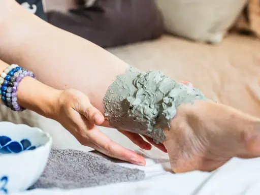Application d'un cataplasme d'argile verte sur une jambe, pour un soin détoxifiant et apaisant.