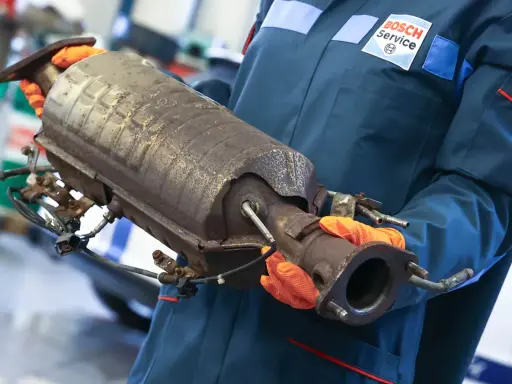 Mechanik w rękawiczkach trzyma zużyty katalizator, prawdopodobnie z Peugeota p2448.