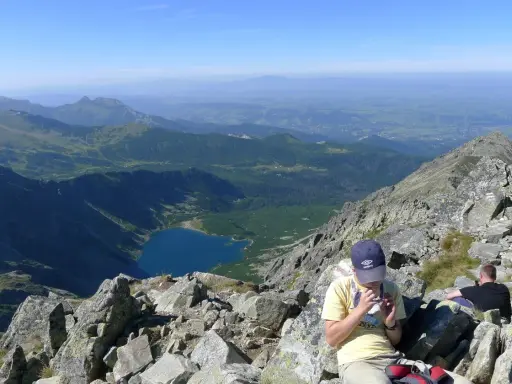 Widok na Tatry z żlebu Kulczyńskiego. W dole jezioro, na pierwszym planie odpoczywający turyści.