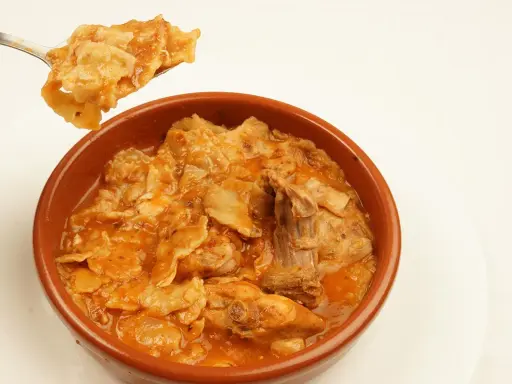 Un plato humeante de comida típica de Albacete, con trozos de carne y pasta en una salsa rojiza.