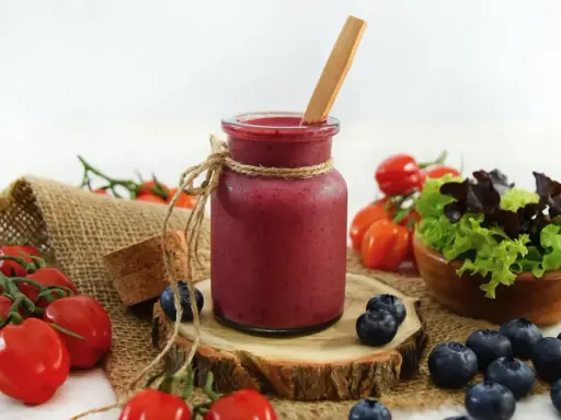 Ein Glas Smoothie, umgeben von frischen Tomaten und Heidelbeeren, die zum Stopfen einladen.