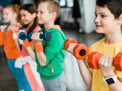 Dzieci ćwiczą z hantlami podczas zajęć si. Uśmiechnięci mali sportowcy budują siłę.