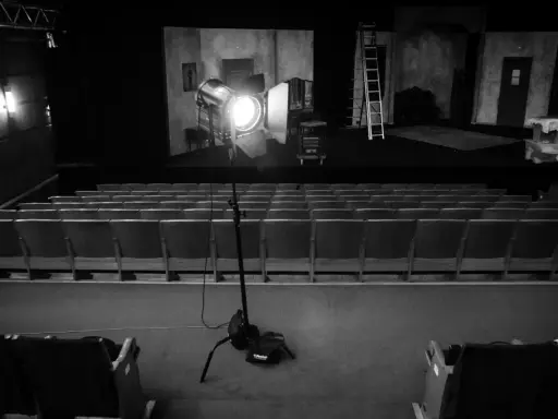 Teatr w czerni i bieli. Na scenie reflektor fresnel oświetla dekoracje, a przed nią puste rzędy siedzeń.
