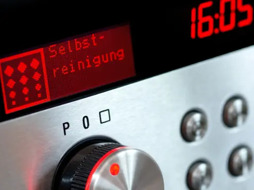 Bedienfeld eines Ofens mit rotem Display, das "Selbst-reinigung" anzeigt. Daneben die Uhrzeit 16:05.