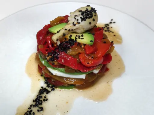Torre de pimientos del piquillo asados, aguacate y queso fresco, coronada con un alcachofa y semillas de sésamo negro.
