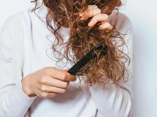 Une personne démêle ses cheveux mouillés et **cheveux emmêlés à la racine** avec un peigne noir.