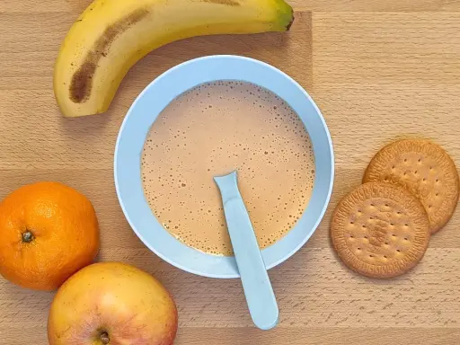 Un tazón de papilla galletas maría con frutas: plátano, naranja y manzana.