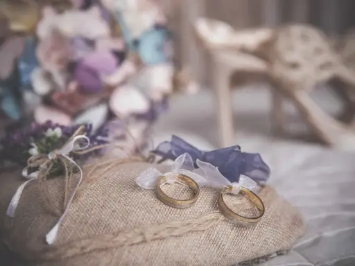 Anillos de boda sobre cojín rústico, ideas para decorar la habitación donde se viste la novia con flores y zapatos elegantes.