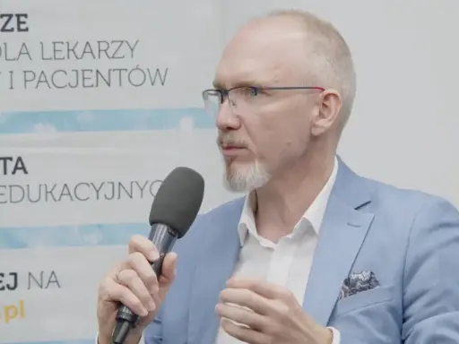 Mężczyzna w okularach i niebieskiej marynarce mówi do mikrofonu, omawiając nowe podejście do leczenia astmy, jakby to był jego własny asthma rap.