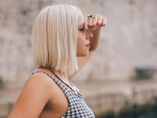 Frau mit blondem **long bob naturwelle** blickt in die Ferne, die Hand schützend über die Augen gelegt.