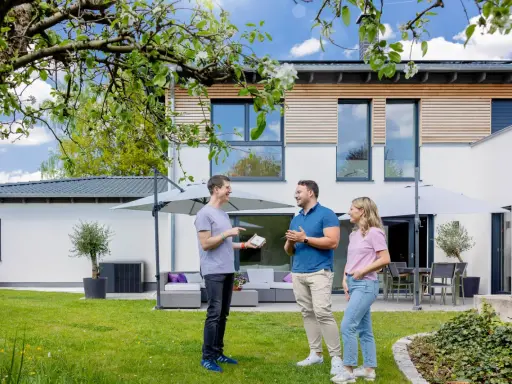 Tre personer diskuterar solcellslösningar på en grönskande trädgård framför ett modernt hus. PFA Solteknik hjälper dig att förverkliga dina drömmar.