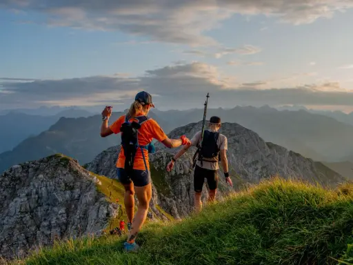 Dwie osoby w sportowym stroju, z plecakami i kijkami, biegną po górskim szlaku. Idealny przykład, jak się ubrać w góry na bieg.