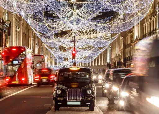 Julbelysning i London i december. Röda dubbeldäckare och taxibilar susar förbi på en livlig gata.