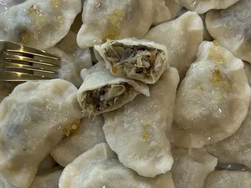 Talerz pełen pysznych, domowych pierogów z kapustą i grzybami. Jeden pieróg jest przekrojony, ukazując bogate nadzienie. Obok leży złoty widelec.