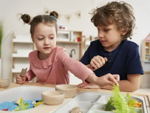 Dwoje dzieci bawi się w piaskownicy sensorycznej z niebieskim piaskiem i roślinami.
