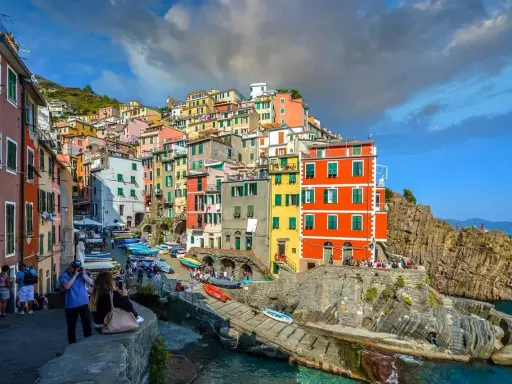 Bunte Häuserfronten der Cinque Terre Orte schmiegen sich an steile Felsen. Boote liegen im türkisfarbenen Wasser.
