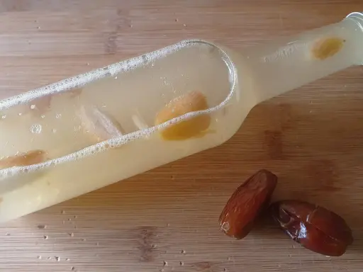 Flasche mit Flüssigkeit und Fruchtstücken, bereit zum Hefe selber machen. Daneben liegen zwei Datteln.