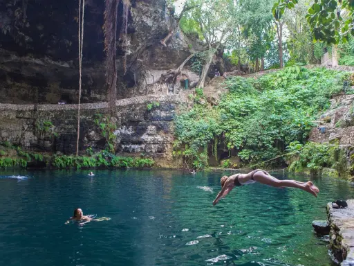 Una ragazza si tuffa nel **cenote Zaci**, un'oasi naturale con acque cristalline e vegetazione lussureggiante.