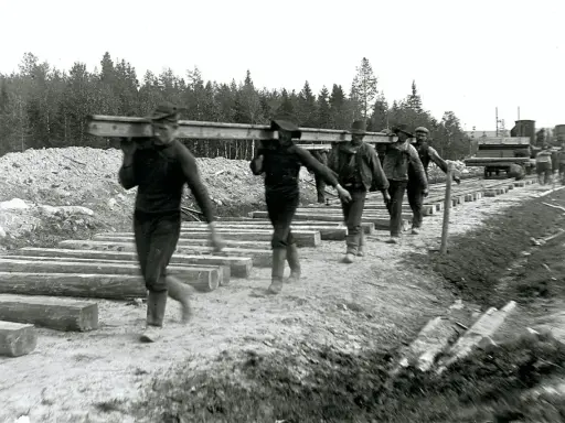 Rallarna i Sverige bär tunga stockar för järnvägsbygge.