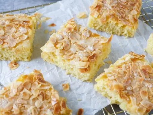 Saftiger Buttermilch Kuchen mit knusprigen Mandelblättchen und Zucker bestreut, auf Backpapier und einem Gitterrost arrangiert.