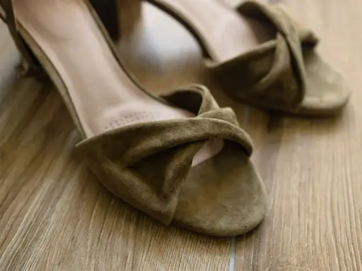 Zamszowe sandały na drewnianej podłodze. Dowiedz się, jak zmiękczyć zamsz po praniu, by znów były jak nowe.