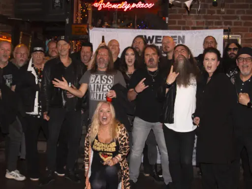 En grupp glada musiker, redo för swedish metal aid. En kvinna i leopardmönstrat poserar i förgrunden.