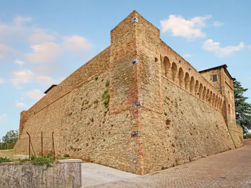 Antica fortezza nella valle del Rubicone, con mura in pietra e mattoni, torri e un loggiato ad archi.