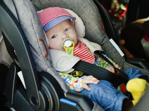 Baby mit Schnuller in Babyschale. Wann wechseln von Babyschale auf Kindersitz? Das Baby ist bereit für den nächsten Schritt.