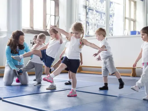 Niños aprendiendo movimientos de **deportes para niños** con una maestra en un gimnasio.