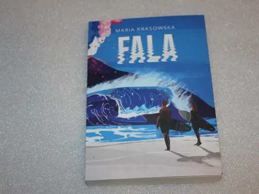 Okładka książki "Fala" Marii Krasowskiej. Dwie postacie z deskami surfingowymi stoją na plaży, patrząc na ogromną falę i wulkan.