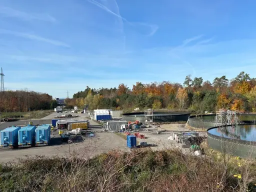 Baustelle mit großen Wasserbehältern und blauen Containern. Hier wird gezeigt, wie funktioniert geothermie mit Erdwärme.