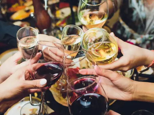 Ręce wznoszą kieliszki z winem, białe i czerwone, do toastu. Rozpoczyna się radosne świętowanie i trawienie alkoholu.