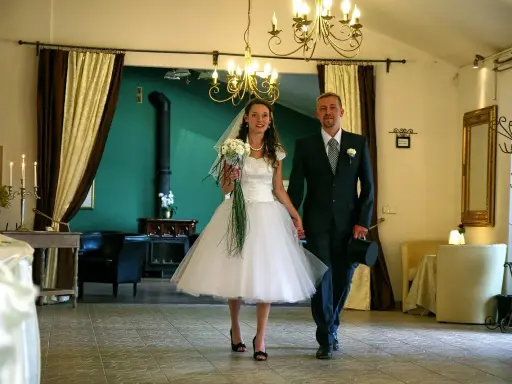 Para młoda idzie ręka w rękę. Panna młoda w sukni w stylu retro, pan młody z cylindrem. Wesele w stylu retro.