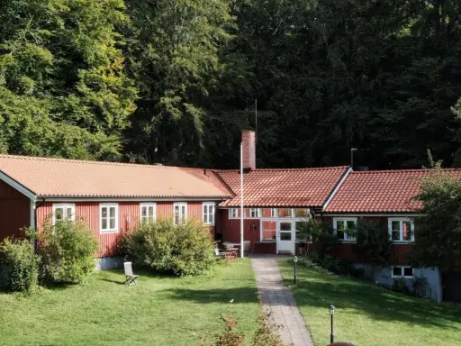 Stocklycke vandrarhem, ett rött hus med tegeltak, omgivet av grönskande träd och en välskött gräsmatta.