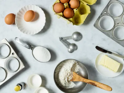 Backzutaten: Eier, Mehl, Zucker, Butter, Muffinförmchen und Messlöffel im amerikanischen Maßsystem.