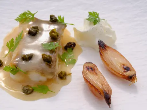 Delicioso lenguado a la meunière con alcaparras, perejil, cebollas caramelizadas y una quenelle de crema.